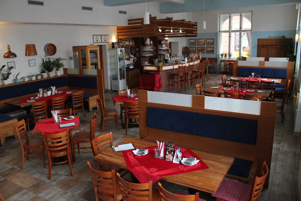 Hlavní sál restaurace s dřevěnými stoly a čepovaným pultem v pozadí